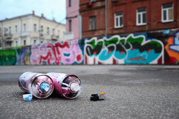Several used spray cans with pink and white paint and caps for spraying paint under pressure is...