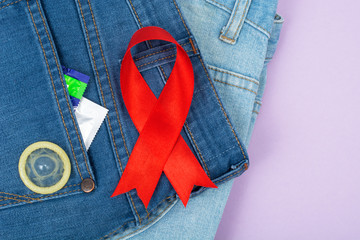 Red ribbon and condom on blue jeans background. Concept of awareness and protection against AIDS, HIV. 1 December