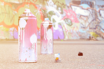 Several used spray cans with pink and white paint and caps for spraying paint under pressure is...