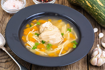 Soup with chicken, pumpkin and noodles on wooden table
