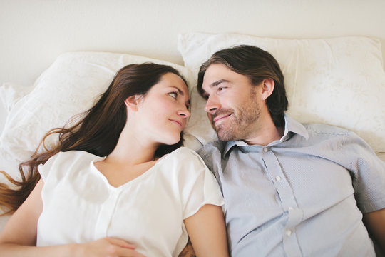 Smiling couple lying on bed, looking in eyes
