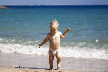 Happy child, adorable blonde toddler boy in diaper, playing on the beach running in the water,...