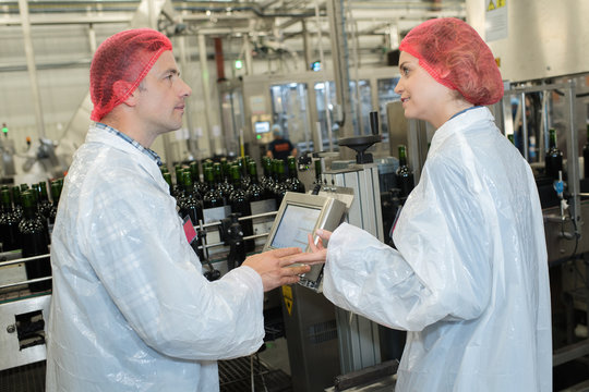 workers in factory checking robotic line for bottling and packing