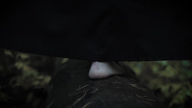 Dressed as a witch woman walks on a log.