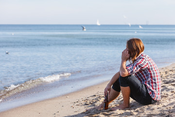 Man depressed with wine bottle sitting on beach outdoor
