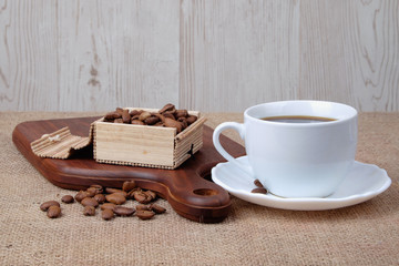 Cup of dark coffee with coffee beans on wooden cutting board . Relax time concept.