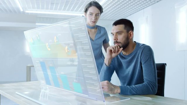 In the Near Future Male and Female Office Workers Discuss Graphical Statistic Shown on Transparent Computer Display. Beautiful People Talking. Interactive Charts on the Screen. 