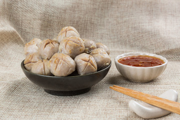 grilled meatballs in a ceramic dish with sweet chilli sauce on calico fabric background, close up.