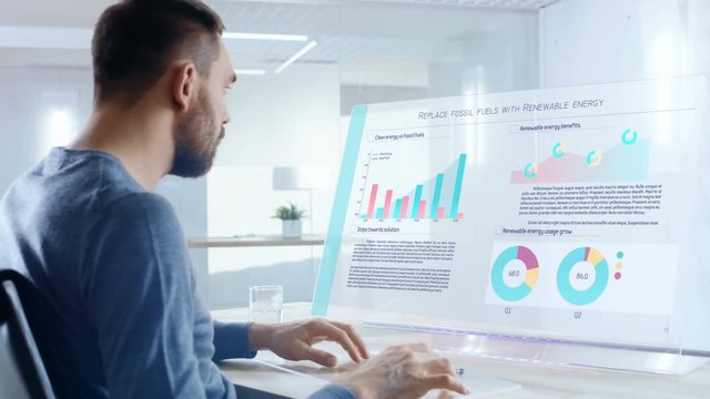In the Near Future Renewable Energy Expert Swipes and Shares Data From Touchscreen Smartphone to His Transparent Display Computer. Screen Shows Interactive Infographics with Colorful Graphs and Data. 