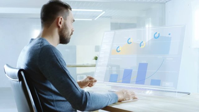 In the Near Future Renewable Energy Scientist Works with Touchscreen Transparent Computer Display. Screen Shows Interactive User Interface with Flowing Pie Charts, Graphs. 4K UHD.