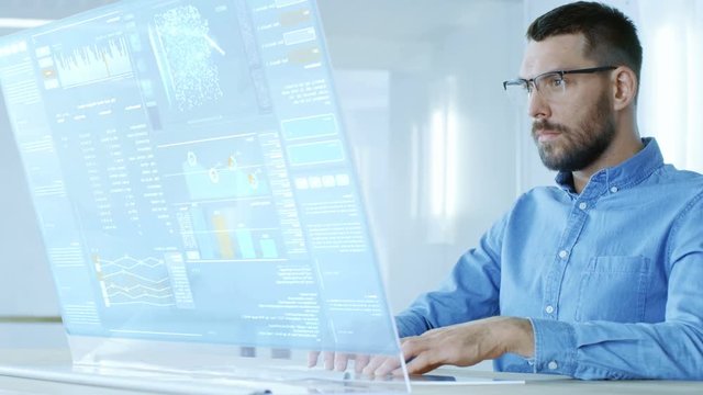 In the Near Future Computer Engineer Works on Computer with Transparent Display. Screen Show Interactive User Interface with Neural Network, Infographics and Charts. 4K UHD.
