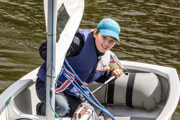 Young sailor on Optimist sailing yacht,  sportive boy having fun on the lake.