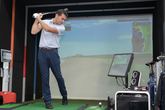 Man practicing golf swing using simulator
