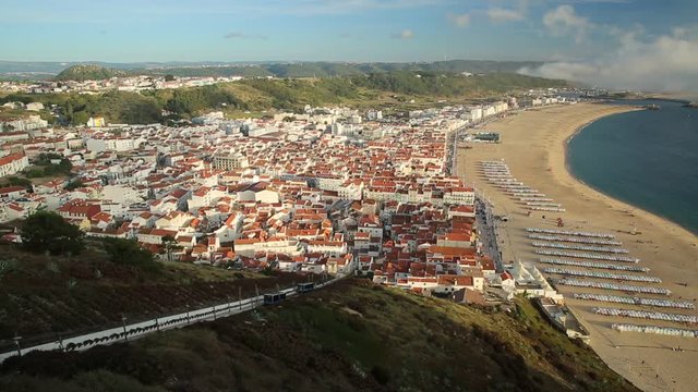 Aerial view slow motion of moving trains of Railway Funicular in skyline and beach waterfront from Miradouro do Suberco in Nazare Sitio, upper town above the giant cliffs in Central Portugal, Europe.