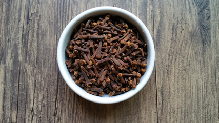 Cloves in white glass bowl on wooden background