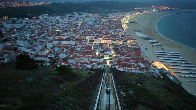 Time lapse panorama of Nazare in Portugal by night, the most popular seaside resorts in Silver Coast. Aerial view of skyline, beach and Ascensor da Nazare or Nazare Funicular from Nazare Sitio
