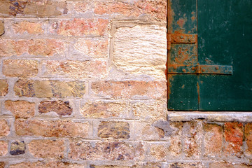 Alte Mauer mit rostigem Fensterladen.
