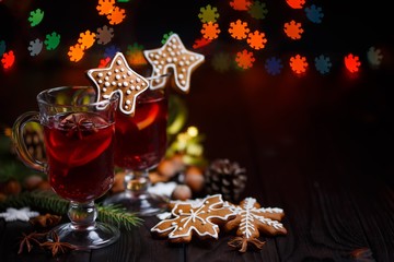 Christmas hot mulled wine with spices and gingerbread cookies on a wooden table and  snowflake shape festive lights, free space for your text design