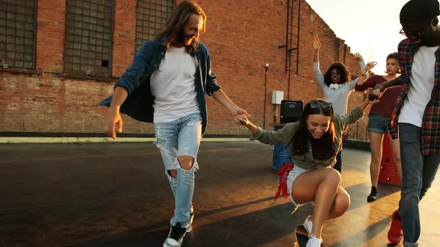 Young men teaching young girl how to skateboarding at the rooftop party. Having fun. The brick wall and funny girls background. Outside. Mixed races