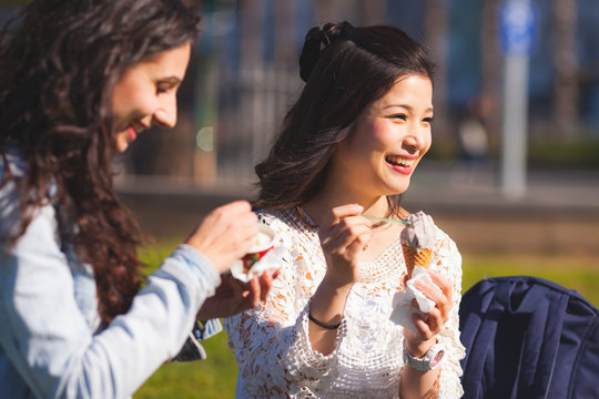 Mixed race girlfriends eating ice cream while having fun outdoors