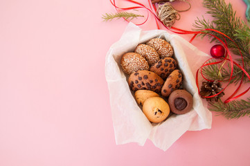 Christmas cookies gift box. Homemade festive baking concept, fir tree branches, balls. Pink background and overhead view.