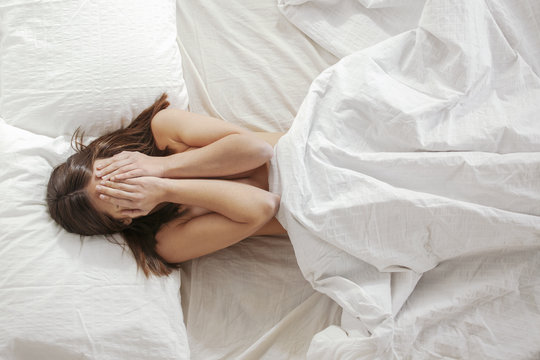 Woman covered her face with hands in a white bed.