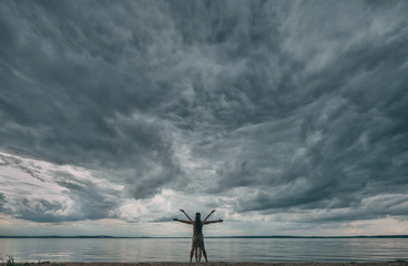 Young man and woman standing in a pose of Leonardo da Vinci Vitruvian Man against dramatic sky.