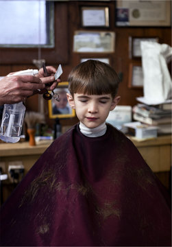 Boy sits quietly in barber's chair as he gets his hair cut