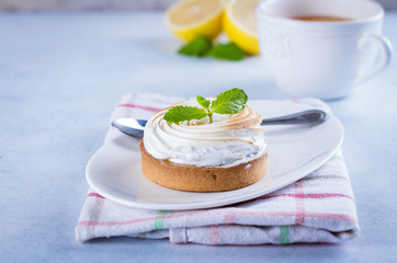 Delicious Lemon tart tartlet with meringue and mint in white plate on blue stone concrete table background. Copy space