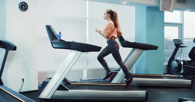 Attractive curly girl running on the treadmill in the sport gym