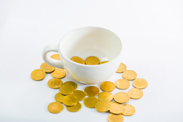 Golden coins in white cup of coffee on the white background.