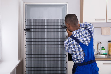 Serviceman In Overall Working On Fridge