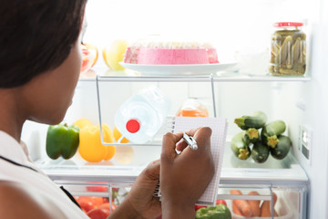 Woman Writing On Spiral Book Near Refrigerator