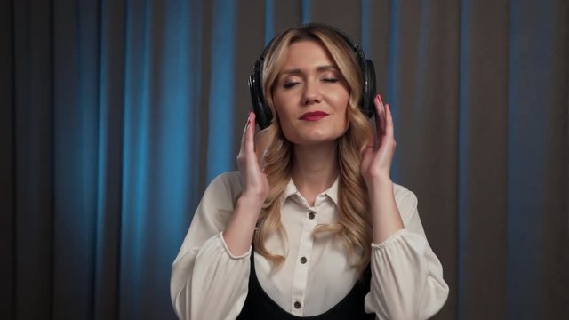 Girl sways to her music with her hands on her headphones and closing her eyes, as she opens them she looks into the camera with a seductive smile, she closes again and knods to the music before