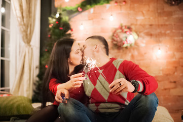 Obraz na płótnie Canvas Male and female hands hold Bengal lights lit. Beautiful happy young family celebrating Christmas together. Lovers on the New Year together in an apartment in the Loft. Bedroom decorated in New Year's