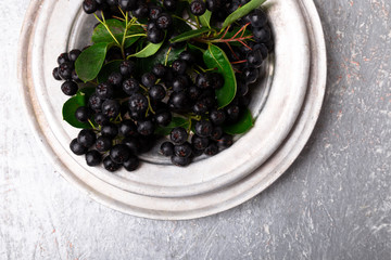 Chokeberry in silver metal bowl on grey background. Aronia berry with leaf. Top view. Copy space.