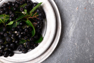Chokeberry in silver metal bowl on grey background. Aronia berry with leaf. Top view. Copy space.