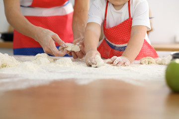 Mother and her cute daughter hands prepares the dough on wooden table. Homemade pastry for bread or pizza. Bakery background