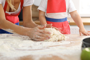 Mother and her cute daughter hands prepares the dough on wooden table. Homemade pastry for bread or pizza. Bakery background
