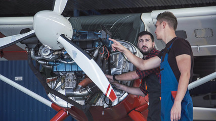 Two mechanics working on a small aircraft in a hangar with the cowling off the engine as they perform a service or repair © Framestock