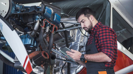 Aircraft mechanic carefully inspecting engine of plane using digital tablet.
