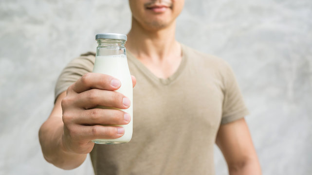 Man holding a bottle of milk on gray background.