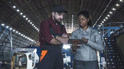 Man discussing over digital tablet in aircraft hangar with woman