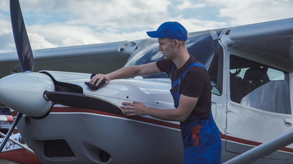 Young pilot or mechanic working on an aircraft wiping down the nose cowling on a small plane parked...