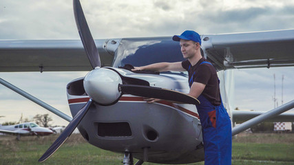 Fototapeta premium Young pilot or mechanic working on an aircraft wiping down the nose cowling on a small plane parked outdoors on an airfield