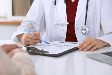 Fototapeta premium Close up of a female doctor filling up an application form while consulting patient