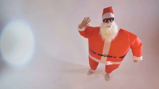 Santa in sunglasses slowly waves both hands. 
