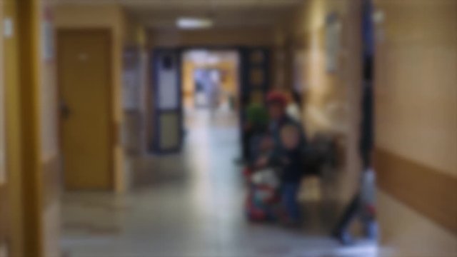 Blurred view of the hospital reception room, people walk in the background.
