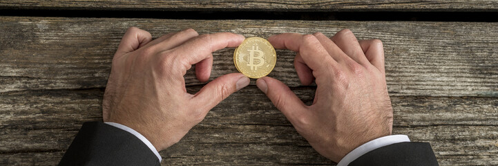 Fototapeta premium Businessman holding one golden Bitcoin in a wide cropped image