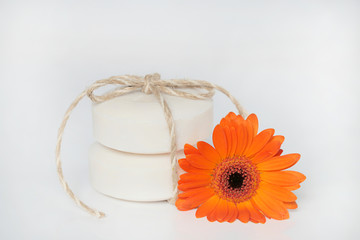 Fototapeta na wymiar flower soap. two white round soap and a orange gerbera flower on a light background. Handmade soap